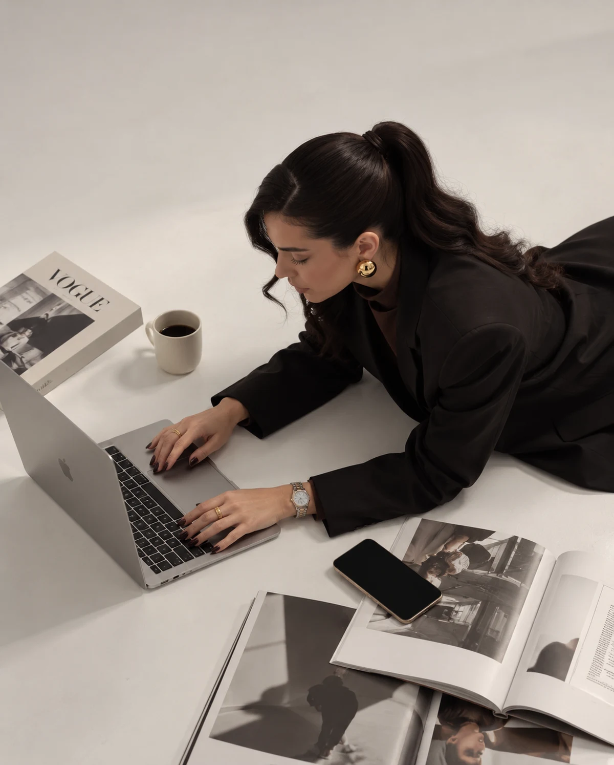 Sabrina Reis trabalhando no laptop, com blazer preto e referências editoriais ao redor.
